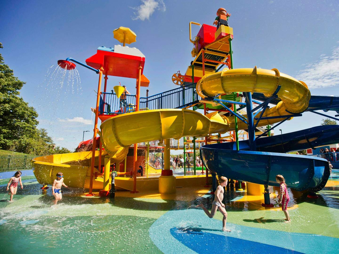 Children playing at a colorful water playground with slides and fountains on a sunny day.