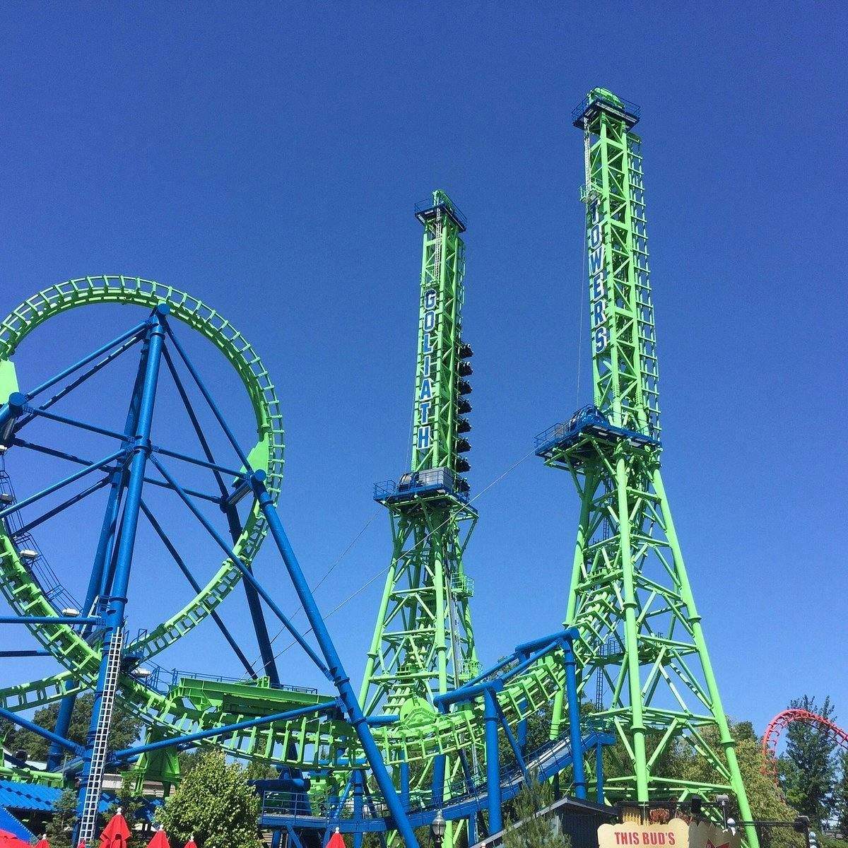 Green and blue rollercoaster with towering structures labeled "Goliath" against a clear blue sky at an amusement park.