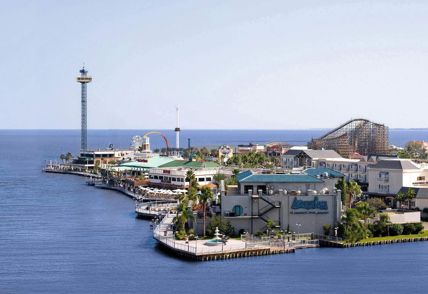 A coastal amusement park with a wooden roller coaster, Ferris wheel, observation tower, and various buildings.