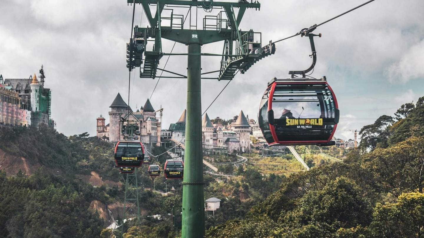 Cable cars over a forested area leading to a castle-like structure in a hilly landscape, labeled 'Sun World Ba Na Hills.'