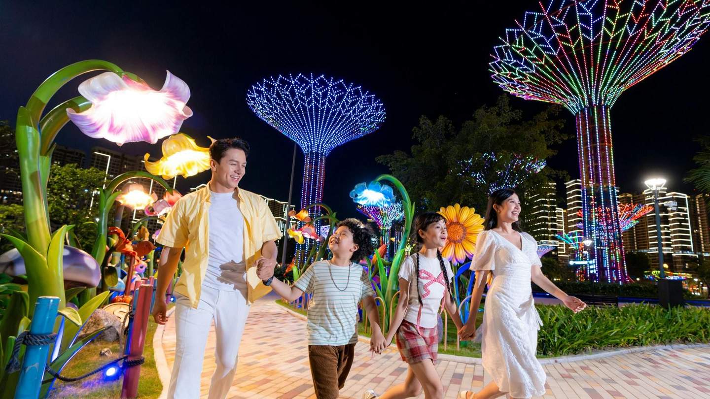 A family holding hands and walking under vibrant illuminated structures and colorful decorative lights at night.