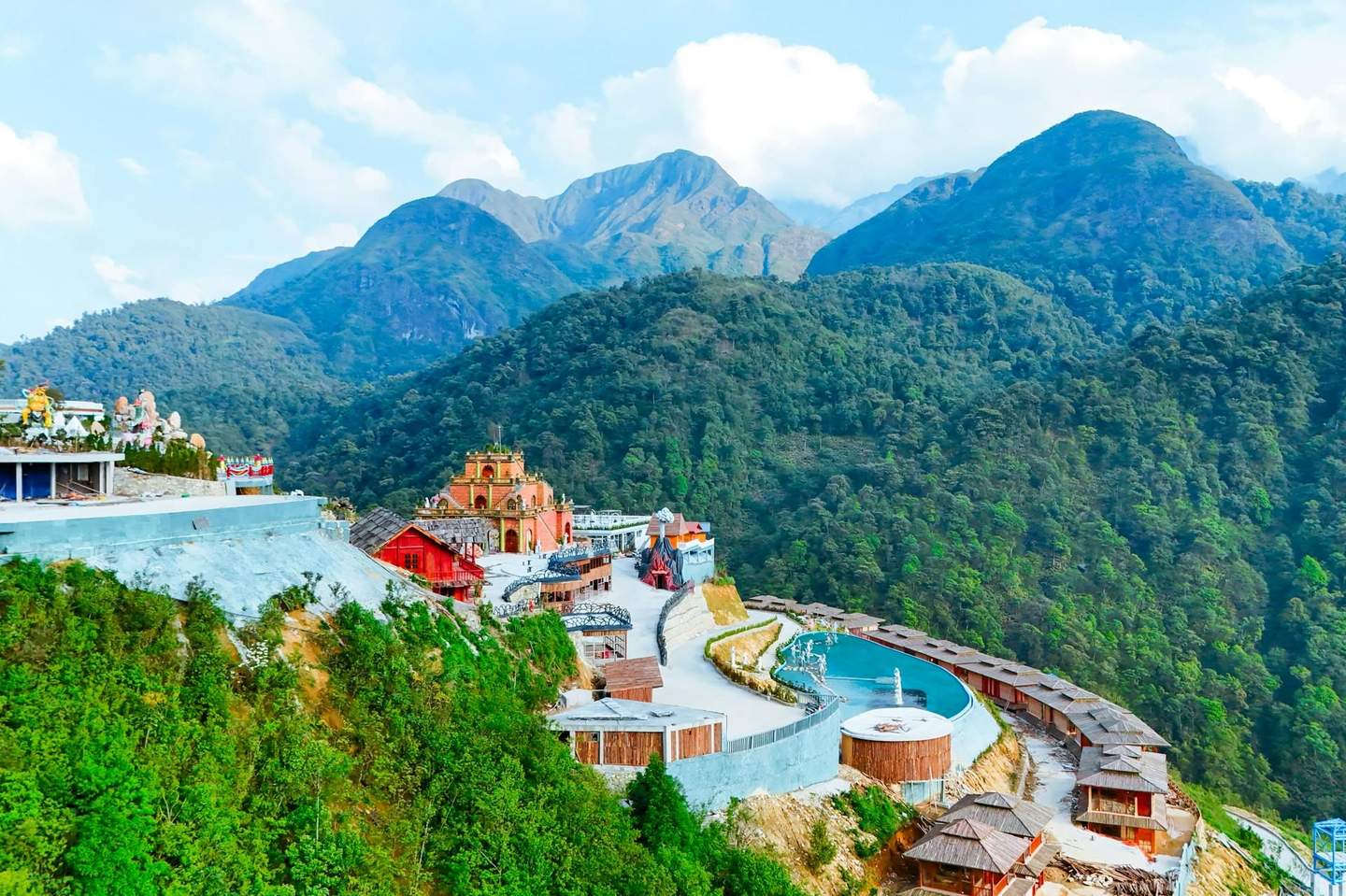 A scenic view of a hilltop resort with colorful buildings, a pool, and lush green mountains in the background.