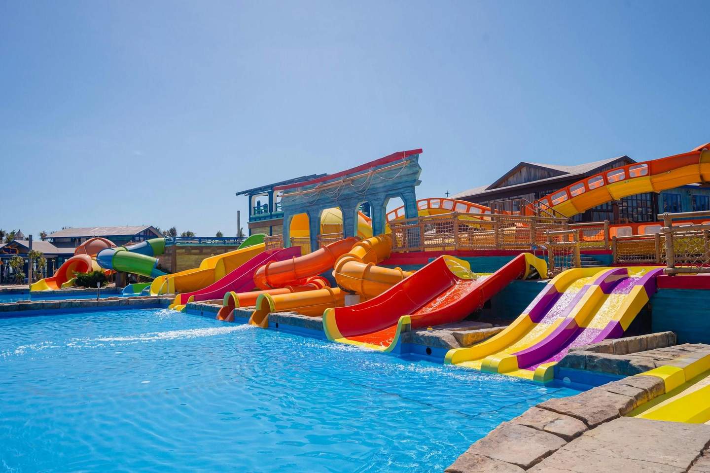 A colorful water park with various slides leading into a pool, under a clear blue sky.