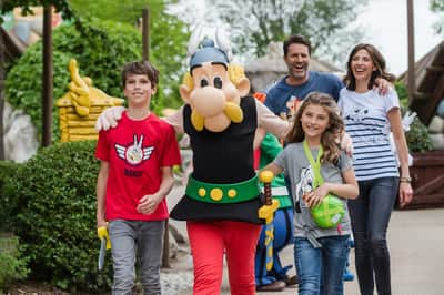 A costumed character with two adults and two children walking outdoors, all smiling and appearing cheerful.