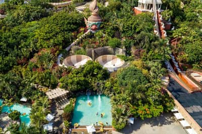 Aerial view of a water park with slides, pool, greenery, and people enjoying various recreational activities.
