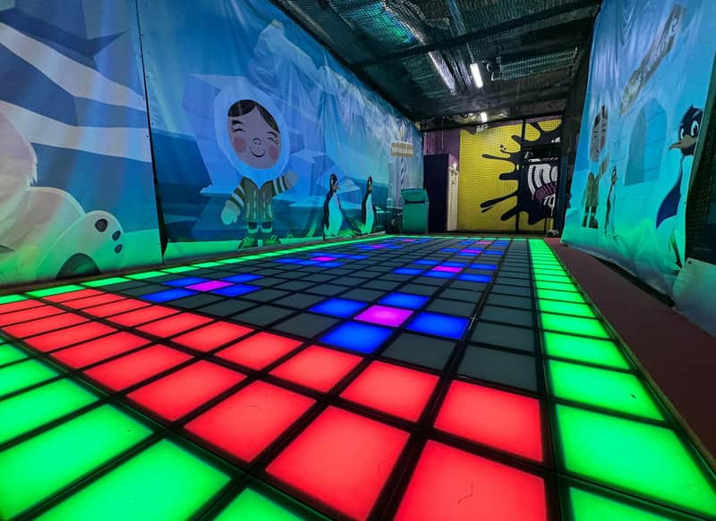 A colorful illuminated dance floor with red, blue, and green lights surrounded by cartoon-themed wall decor.