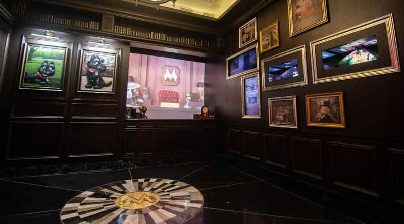 A themed room with dark wood paneling, framed pictures on the walls, and a projection of an animated scene on display.