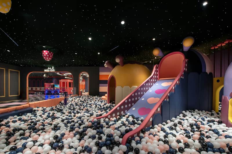 Indoor playground with colorful slides, dome structures, and a ball pit under a ceiling with star-like lights.