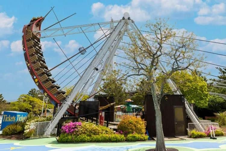 A pirate ship ride at an amusement park, surrounded by trees, flowers, and a clear sky in the background.