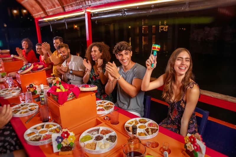 A group of people sitting at a table with food and drinks, one holding a colorful maraca, smiling and enjoying themselves.