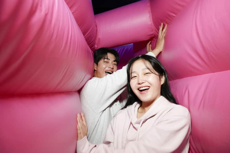 Two people smiling inside a pink inflatable structure, one wearing a light sweatshirt and the other a pink hoodie.