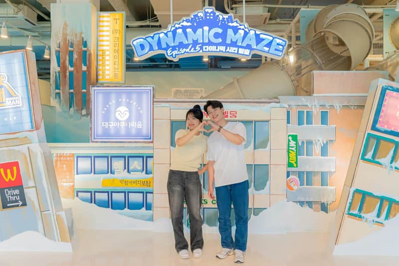 Two people stand together, smiling and forming a heart with their hands in front of a "Dynamic Maze" sign and themed decor.