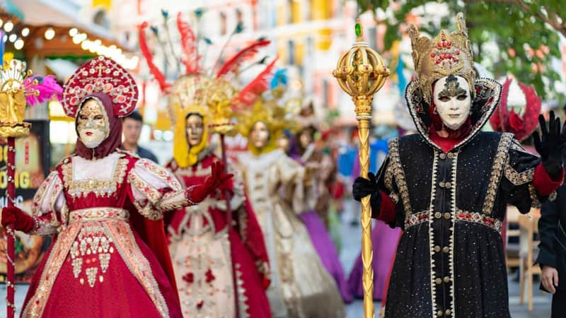 People in elaborate, colorful costumes and masks participate in a festive parade or celebration.
