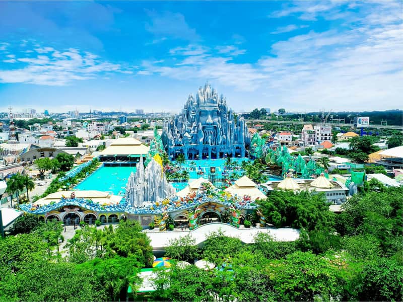 A large theme park with a mountain-shaped structure featuring a face, surrounded by greenery and pools under a blue sky.