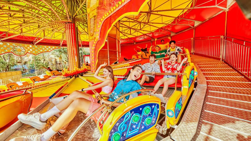 People enjoying a colorful amusement park ride under a bright canopy, laughing and raising their hands.