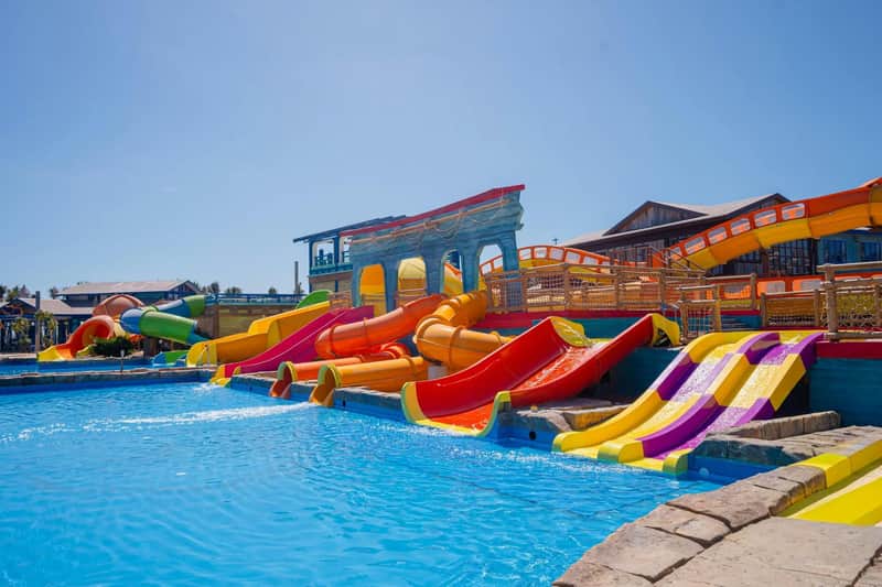 Colorful water slides leading into a pool at an outdoor water park with clear skies in the background.
