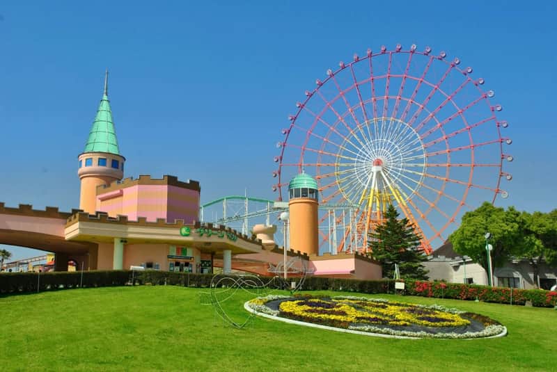 An amusement park with a large Ferris wheel, a colorful castle-like building, and landscaped gardens under a clear blue sky.