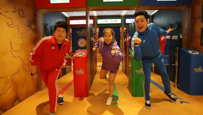 Three people in colorful tracksuits pose enthusiastically in a themed indoor setting with vibrant decor and props.