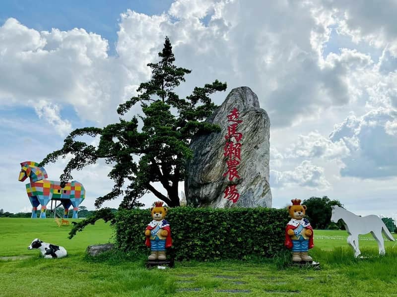 A grassy park scene featuring a large colorful horse statue, a stone with red writing, and two bear statues in regal attire.