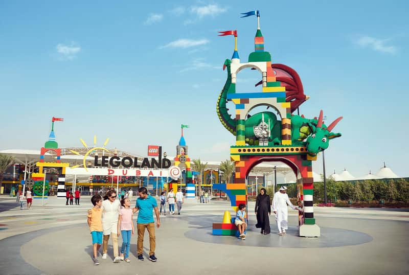 Families walk near the colorful entrance of LEGOLAND Dubai, featuring a large LEGO dragon and vibrant archway under a clear sky.