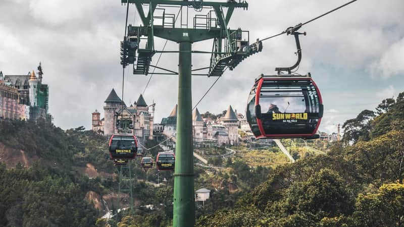 Cable cars over a forested area leading to a castle-like structure in a hilly landscape, labeled 'Sun World Ba Na Hills.'