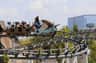 People riding a detailed, dragon-themed rollercoaster on a sunny day with trees and a building in the background.