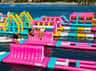 Des personnes s'amusant dans un parc aquatique gonflable haut en couleur, avec des toboggans et des obstacles, qui flotte sur un lac.