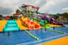 Niños jugando en un colorido parque acuático con múltiples toboganes y una piscina, bajo un cielo nublado.