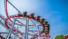 A rollercoaster with orange cars and people riding on red tracks against a clear blue sky.