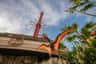 A statue of a flying dinosaur with orange wings is in front of an amusement park entrance, with a tall red ride visible in the background.