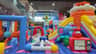 Indoor inflatable play area with colorful slides, tunnels, and animal-themed bouncers under a high ceiling.