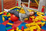A young girl swings on a red ball in an indoor play area filled with large yellow and red building blocks.