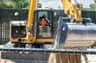 A child and an adult in a construction vehicle cabin. The child wears a safety vest, and the vehicle has a visible bucket.