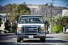 A van with passengers inside is driving on a street, with the Hollywood sign visible on a hill in the background.