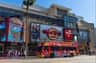 A red sightseeing bus parked in front of the Hard Rock Cafe and TCL Chinese Theatre on a sunny day.