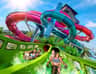 Four people descending a green waterslide with intertwined red, blue, and purple slides in the background under a clear blue sky.