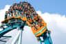 A group of people riding a large rollercoaster, descending a steep drop, all wearing safety harnesses and looking excited.