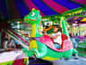 Child riding a green dragon ride at an amusement park, smiling and holding the handlebars. Colorful canopy overhead.