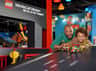 A man and a boy happily race colorful LEGO cars on a track in a playful, brightly-lit indoor environment.