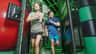 Two people running and smiling inside an indoor obstacle course with green and black structures.