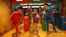 Three people in colorful tracksuits pose enthusiastically in a themed indoor setting with vibrant decor and props.