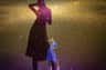 A person in a blue dress poses dramatically against a textured backdrop, with their shadow projected behind them.