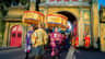 A traditional procession with participants in colorful attire carrying ornate canopies, passing through an ancient gate.