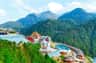 A scenic view of a hilltop resort with colorful buildings, a pool, and lush green mountains in the background.